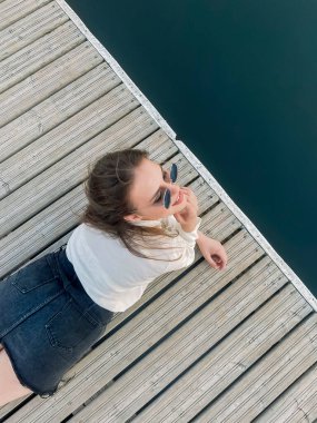 Genç esmer kadın rıhtımda yatıyor ve yaz günü temiz göl suyu sıçrıyor.