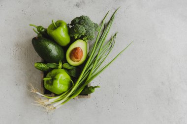 Gri arka plandaki konteynırın içine yerleştirilmiş çeşitli taze sebzelerin üst görünümü