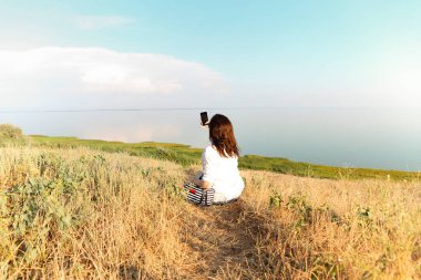 Kurumuş tarlada oturan ve hafta sonu kırsal kesimde dinlenirken akıllı telefonun fotoğraf çektiği arka plan görüntüsü.