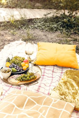 Bahçedeki romantik piknik sırasında yastıklı çeşitli olgun meyvelerle birlikte masaların yanına yerleştirilmiş bir çift şarap bardağı.