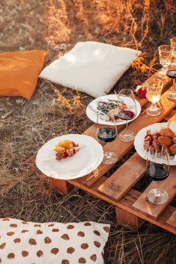 Şenlikli sonbahar pikniği sırasında çimenli çayırlarda çiçek aranjmanlarıyla ahşap masaya yerleştirilmiş zarif cam eşyalar.