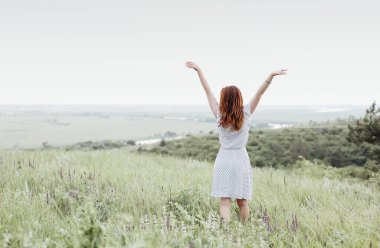 Doğada yaz günü çimenlerin üzerinde kızıl saçlı genç bir kadın.