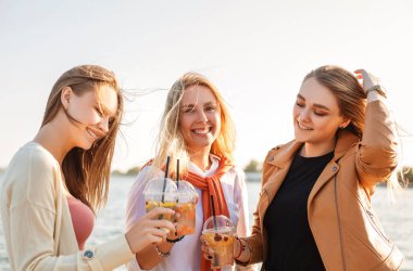 İçki ısmarlayan mutlu genç kadınlar kaldırımda yürüyor ve güneşli bir hafta sonu gününde sokaklarda gülümsüyor.