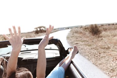 Yolculuk sırasında Cabriolet 'in yolcu koltuğunda oturan yaz kıyafetleri içinde neşeli genç bir kadın.