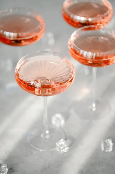 Top view of glasses with cold pink champagne placed on table near cubes of ice during party on summer day