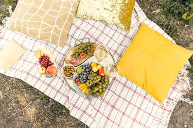 Bahçedeki romantik piknik sırasında yastıklı çeşitli olgun meyvelerle birlikte masaların yanına yerleştirilmiş bir çift şarap bardağı.