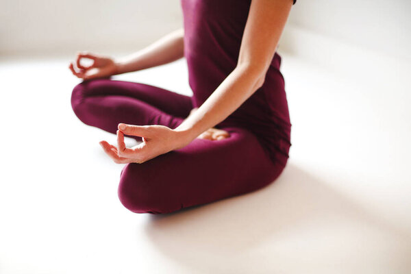 Young female in yoga pose and meditating in white room