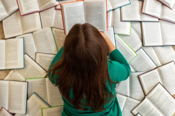 Вид анонимной студентки, лежащей на книгах и читающей во время подготовки к экзамену