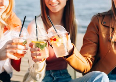 İçki ısmarlayan mutlu genç kadınlar kaldırımda yürüyor ve güneşli bir hafta sonu gününde sokaklarda gülümsüyor.