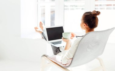 Çıplak ayaklı, elleri başının arkasında oturan ve evdeki ışık odasında dizüstü bilgisayar kullandıktan sonra gözleri kapalı dinlenen genç bir kadın.