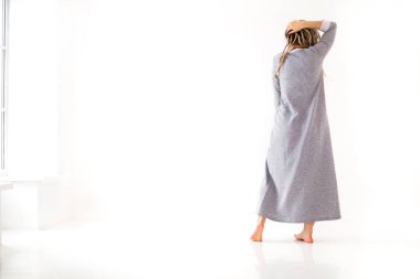 Beyaz arka planda izole edilmiş bej elbiseli, titrek saçlı neşeli genç bir kadın.