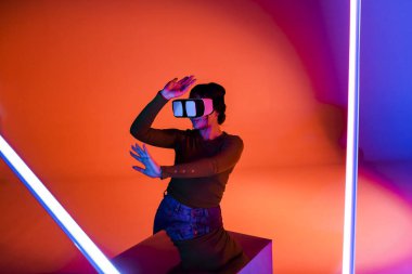 VR kulaklıklı mutlu kadın gelecekteki odada kırmızı neon ışığı altında gülümseyip sanal gerçekliği keşfediyor.