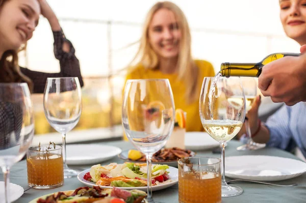宴会期间 快乐的男男女女一边坐在餐桌旁 一边微笑着等待侍者端着酒杯倒酒 — 图库照片
