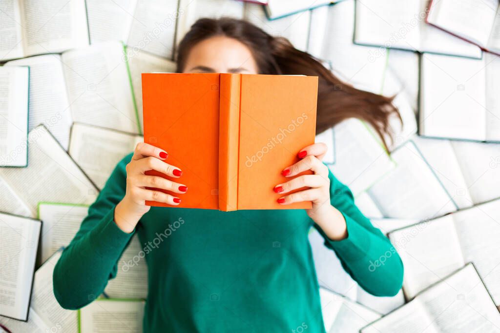 Top view of anonymous female student lying on books and reading during exam preparation