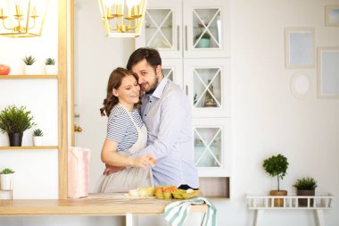 Mutfakta birlikte yemek pişirirken birbirlerine sarılan mutlu çiftin yan görüntüsü.