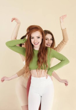 Neşeli genç kız arkadaşlar gülümsüyor ve bej arka planda sarılırken kameraya bakıyor.