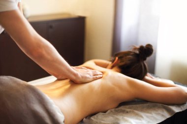 Meçhul usta spa salonundaki masada uzanan anonim kadına sırt ve omuz kası masajı yapıyor.