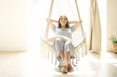 Hayalperest kadın sallanan sandalyede uzanıyor ve güneşli sıcak odada hafta sonunun tadını çıkarıyor.