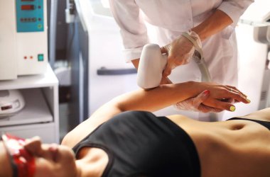 Yukarıdan gelen kadın müşterinin lazer epilasyon sırasında güzellik salonunda kanepede uzanması.