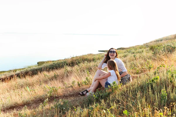 笑顔の母と娘は田舎で一緒に週末を過ごしながら花の草原で優しく抱き合ってカメラを見て — ストック写真