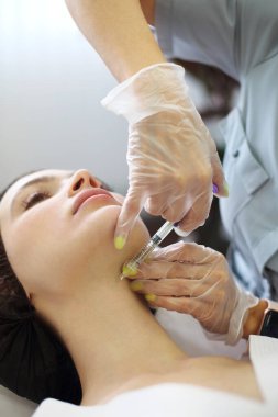 Güzellik uzmanının güzellik kliniğinde yaşlanmayı önleyen bir prosedür sırasında kadının gözlerinin yanında hyaluronik asit enjekte etmesi.
