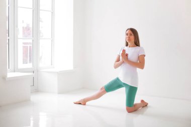 Spor giyim bölümünde sakin bir kadın dengede durup başka tarafa bakarken yoga yapıyor.