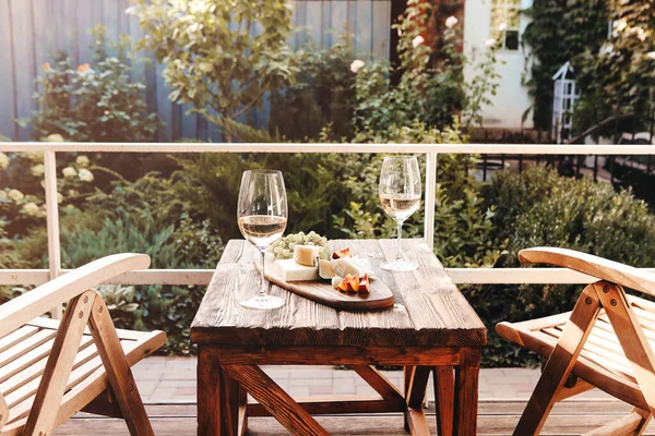 Güneşli bir yaz gününde terasta sandalyelerin yanına meyve ve peynir konmuş şarap kadehleri.