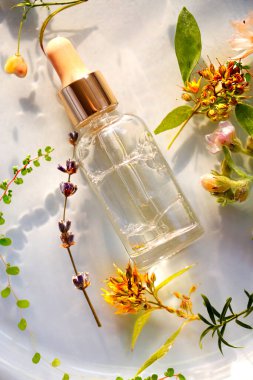 Beyaz arka planda taze çiçeklerin yanına yerleştirilmiş kaplıca oturumu için gerekli aromatik yağ içeren cam şişe üst görünümü