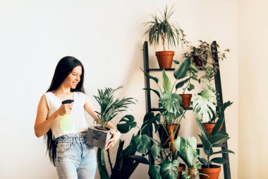 Saçları örgülü genç bir bayan hafta sonu evde bahçeyle uğraşırken gülümsüyor ve saksı bitkileriyle ilgileniyor.