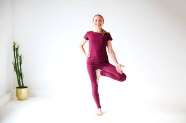 Spor giyinen sakin bir kadın Firefly pozunda yoga yapıyor dengede duruyor ve başka tarafa bakıyor.