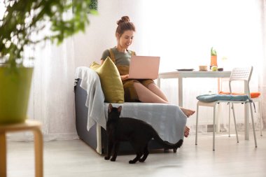 Masanın yanındaki koltukta oturan çıplak ayaklı genç bir kadın ve evde sabahları netbook okuyor.