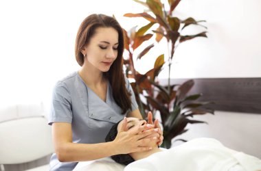 Genç bir kadın kuaförde kozmetik uzmanı tarafından kafa masajı yaptırıyor, sabahlık giymiş, kaplıca salonunda duruyor ve kadın müşterinin yüzüne masaj yaptırıyor.