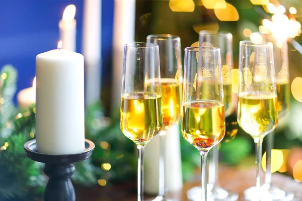 一套香槟酒杯放在木制桌子上 上面点缀着蜡烛 墙上挂着模糊的圣诞树 — 图库照片