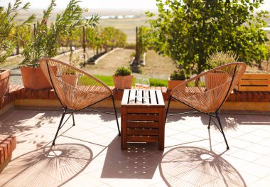 Kırsal ahşap masada iki bardak beyaz şarap ve terasta saksılar güneşli yaz sabahlarında üzüm bağları tepeleri manzarasıyla birlikte dışarıda.