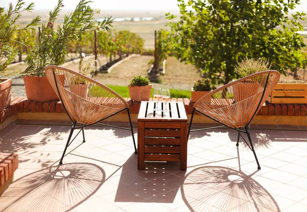 Kırsal ahşap masada iki bardak beyaz şarap ve terasta saksılar güneşli yaz sabahlarında üzüm bağları tepeleri manzarasıyla birlikte dışarıda.