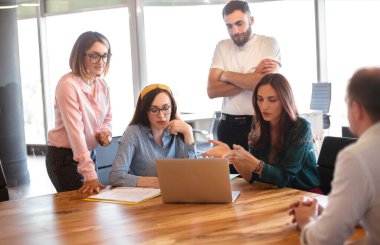 Modern iş yerindeki toplantı sırasında sandalyede oturan ve işçilerle konuşan şık giyimli bir kadın.