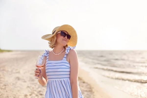 海の近くの砂浜でワインを楽しみながら笑顔と離れて見て夏の衣装で幸せな大人の女性 — ストック写真