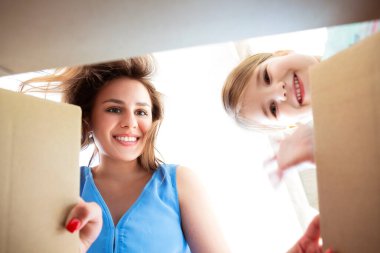 Heyecanlı anne ve şirin küçük kız kutunun içine bakıyor, mutlu esmer anne ve güzel kız kutuyu açıyor ve gülümsüyor. Aşağıdan görüntü görüntüsü. Paketleri açma, yer değiştirme ve taşınma günü konsepti