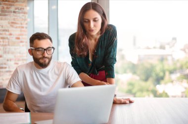 Modern ofis içinde iş projesi ve finansal sunum üzerinde çalışan iki genç düşünceli iş arkadaşı, girişimci erkek ve kadın onun yanında düşünceli bir şekilde dizüstü bilgisayara bakıyorlar.