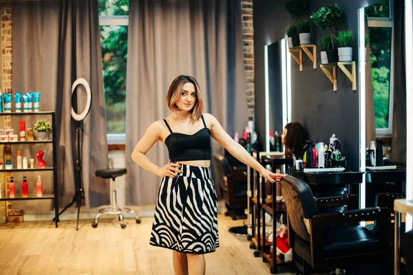 現代的な美容室のインテリアでポーズをとるプロの若い美しい女性の美容師 笑顔と鏡の横に椅子に保持しながら カメラを見て 中小企業起業家のコンセプト — ストック写真
