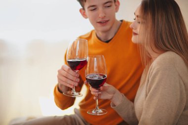 Genç adam ve kadın evde romantik bir buluşma sırasında sarılıp kırmızı şaraptan zevk alıyorlar.