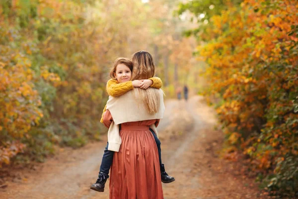 秋の森の中を歩いていると お母さんと子供が手を取り合って黄色の木の葉で覆われた道を歩き 美しい自然の中で時間を過ごす — ストック写真