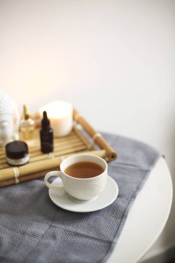Spa salonundaki yuvarlak masa, bambu tepsisinin yanında bir fincan bitki çayı, değişik aromatik yağlar ve kremler, rahatlama prosedüründen sonra hazırlanmış, beyaz duvar arkasında izole edilmiş.