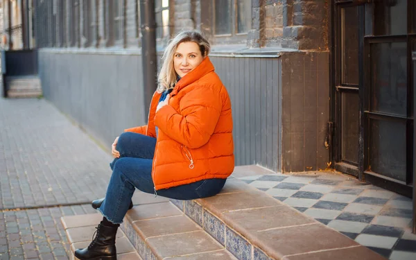 Glücklich Lächelnde Frau Mittleren Alters Orangefarbener Daunenjacke Sitzt Draußen Auf — Stockfoto