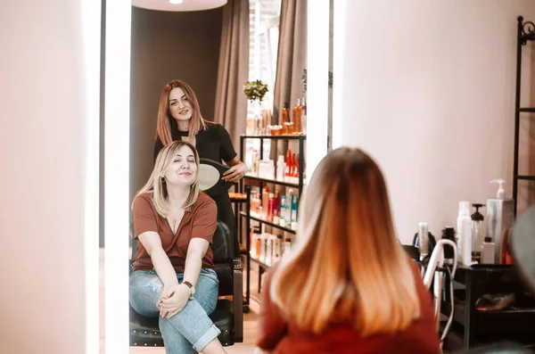 若い美しい長い髪のブロンドの女性は彼女のヘアスタイリストに鏡に笑顔 美容サービス ライフスタイルコンセプト — ストック写真
