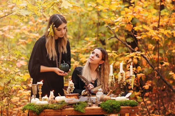 秋の森の中で魔法の食材とテーブルに座って魔女の衣装の若い女性 — ストック写真