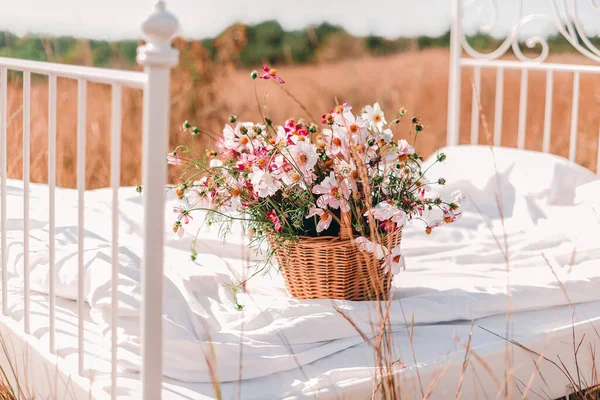 晴れた夏の日に穀物小麦の夏のフィールドや牧草地できれいな白い寝具とベッドの上にウィッカーバスケットの多くの美しいカラフルな野の花 選択的なフォーカス — ストック写真