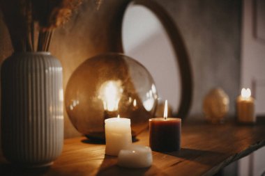 Ahşap raftaki yuvarlak ayna, yanan iki mum ve küçük porselen Buda kafası minimalist modern apartmanın arka planındaki beton duvarın üzerine yansıyan aynalı bir yüzey.