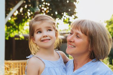 Mutlu orta yaşlı büyükanne, küçük şirin bir anaokulu torununu kucağında tutarken yaz günü bahçede dururken, büyükannesi ve küçük kızı kırsalda birlikte vakit geçiriyorlar. Aile kavramı
