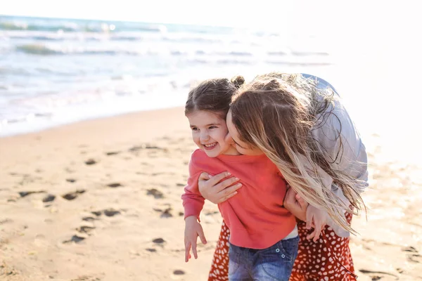 笑顔の娘と一緒に夏の海辺で一緒に過ごす時間を楽しんで 日当たりの良いビーチで彼女に向かって実行している若い愛情のある母親 幸せなお母さん抱擁の女の子 — ストック写真